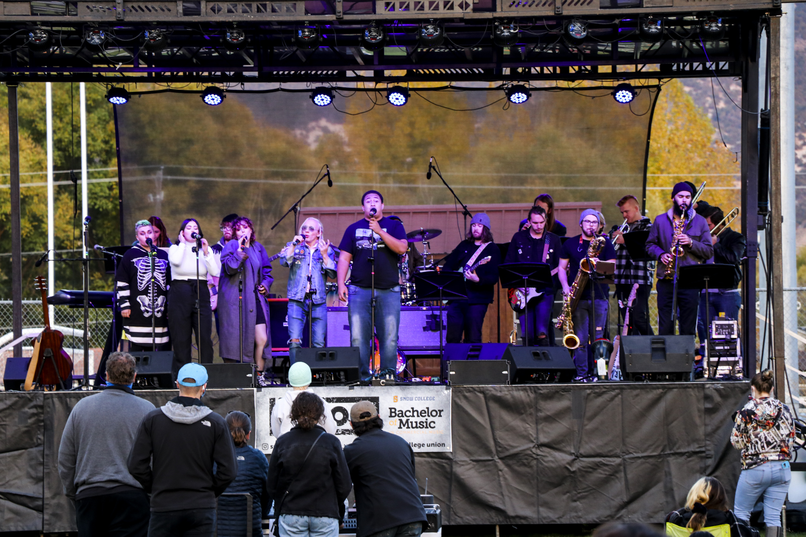 Snow College students singing and playing instruments on an outside stage with an audience watching