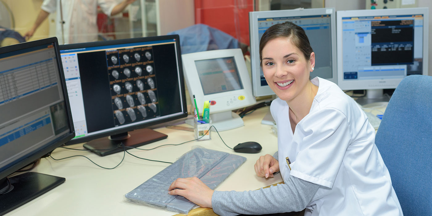Woman in scrubs sitting at a computer with brain scans on the moniter.