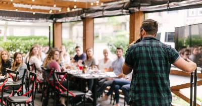 A speaker talking to an audience in an open air cafe style setting.